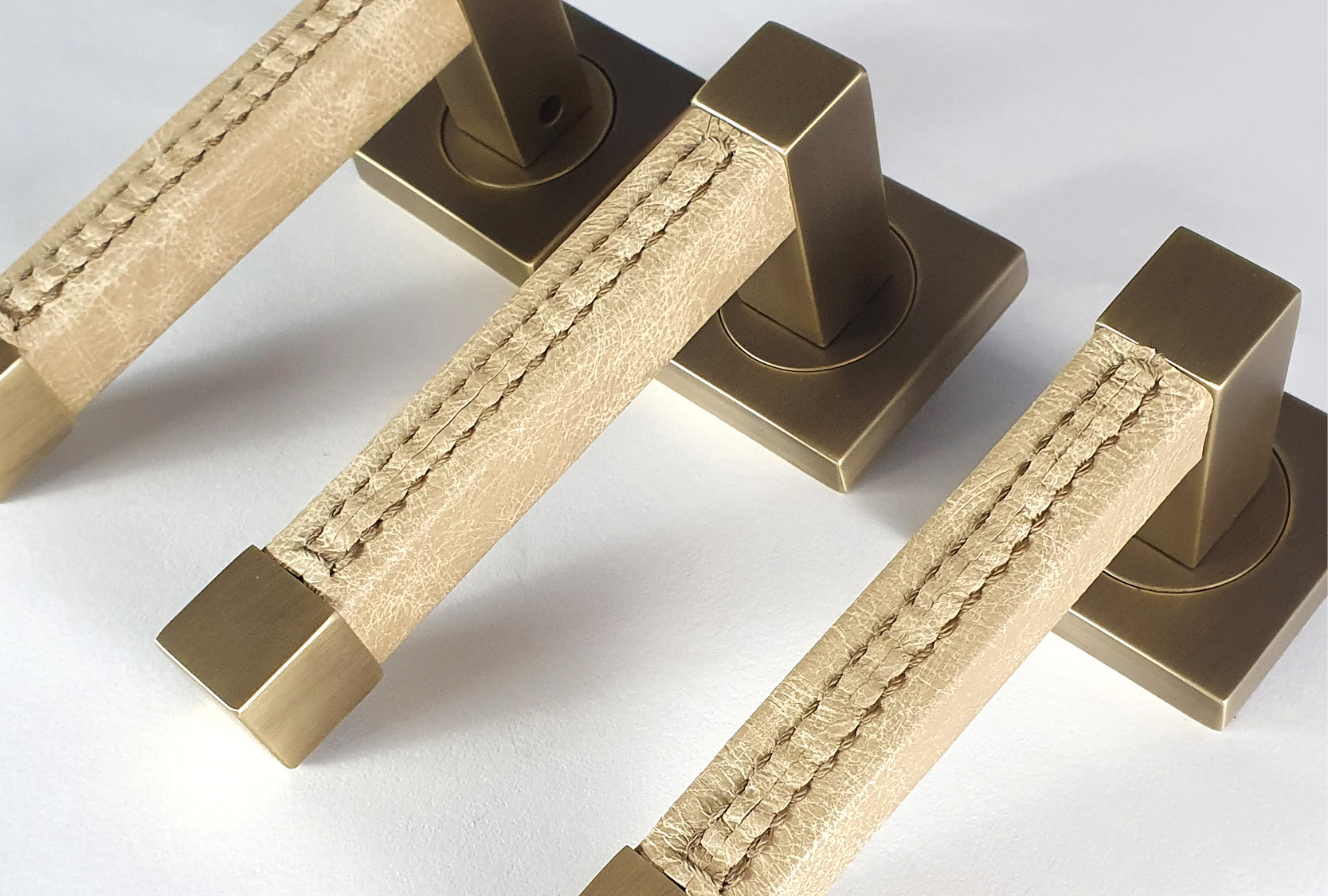 Image displays three custom square door levers. The grip has a custom leather and a custom stitch. The metal is finished in a fine antique.