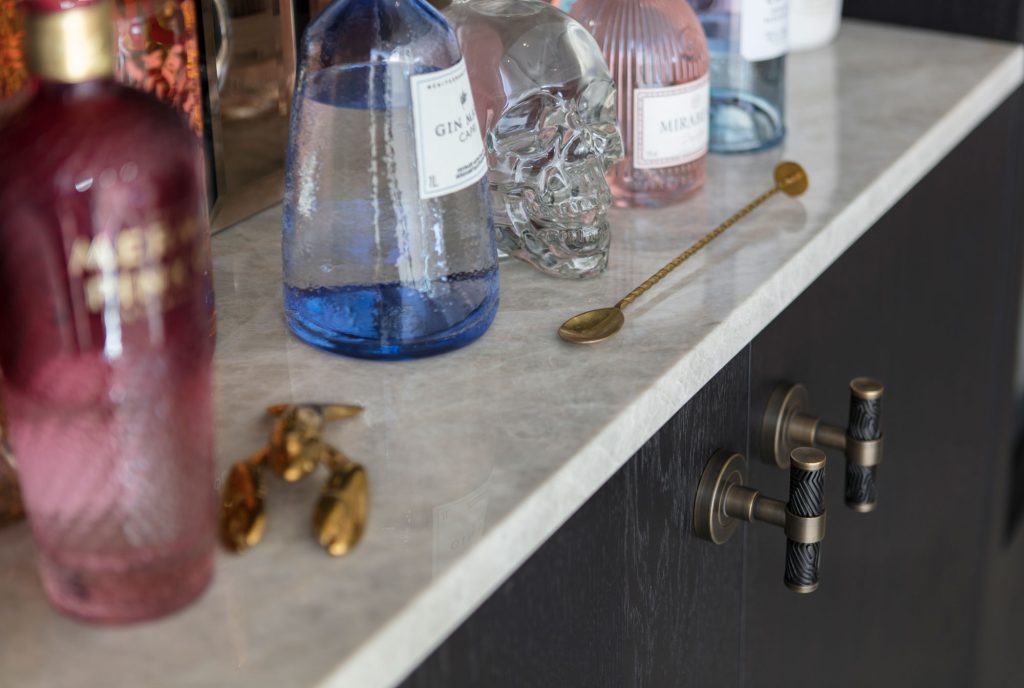 A home bar complete with impressive spirit collection. The built in cupboards for this bar use Turnstyle Designs Labyrinth T Bar pulls, an intricate and decorative t bar a handle finished in Black Bronze Amalfine with Fine Antique Brass metal. The deep browns and brass colours against the dark moody oak of the cupboards doors creates a beautiful contrast.