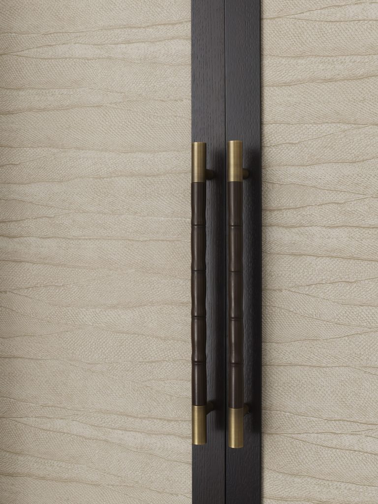 Two cupboard pull handles on custom made furniture by AG Meridian Joinery. The doors are panelled with textured fabric. The handles are from Turnstyle Designs and a Bamboo grip design in Cocoa with Fine Antique Brass.