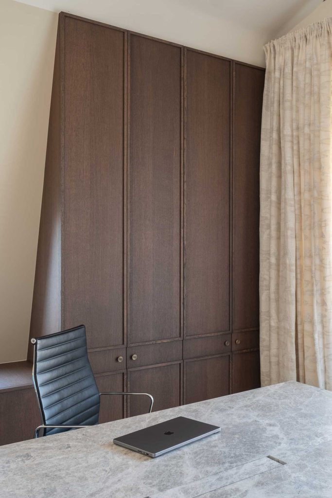 Decorative circle brass cabinet knobs by Turnstyle Designs have been used on modern panelled cupboard doors in this office room. Browns and neutral colours have been used with accents of black from the leather office chair.
