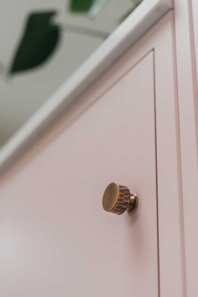 A hand hammered cabinet knob on a soft pink cabinet door. This quality brass cabinet knob has been hand made by Turnstyle Designs, a luxury British hardware brand.