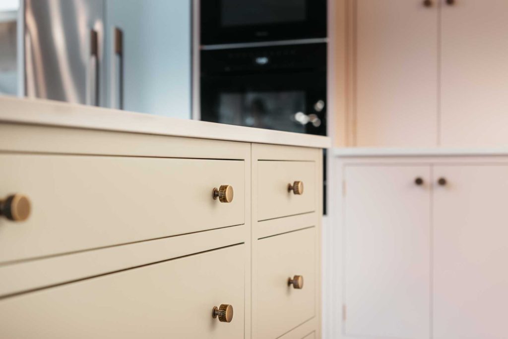 Hand hammered cabinet knobs on a soft pink kitchen island unit with long drawers. The hammered cabinet knobs are from luxury hardware specialists Turnstyle Designs.