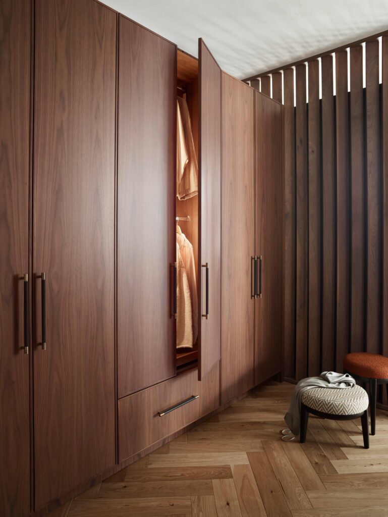 Large built in wardrobe with Turnstyle Designs handstitched leather pull handles. The dark wood wardrobe sits on parquet flooring with decorative wooden panelling alongside.