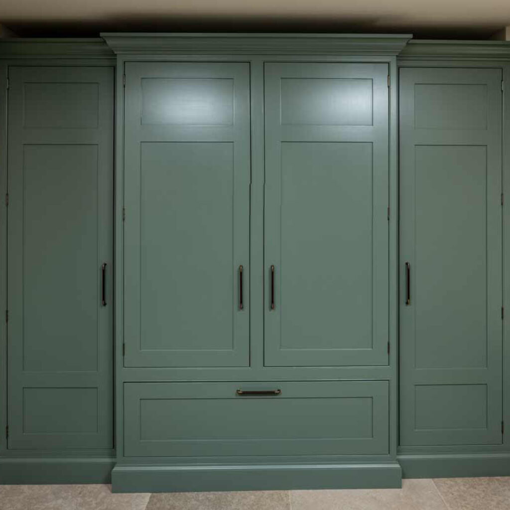 Large bespoke cabinet in a luxury boot room. Used for storage and finished in the same colour and the surrounding cabinets and decorative wood panneling.