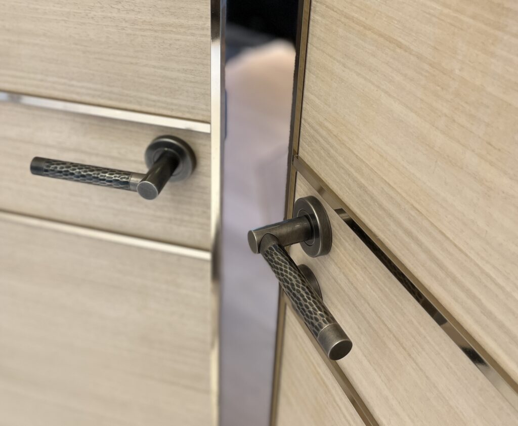 A pair of hammered brass door levers on double entrance doors. The door levers are made by Turnstyle Designs.