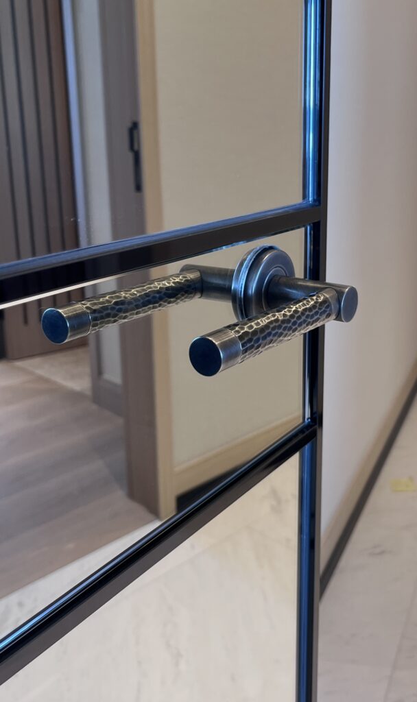 Hammered door lever by Turnstyle Designs fixed on a modern style glass door.