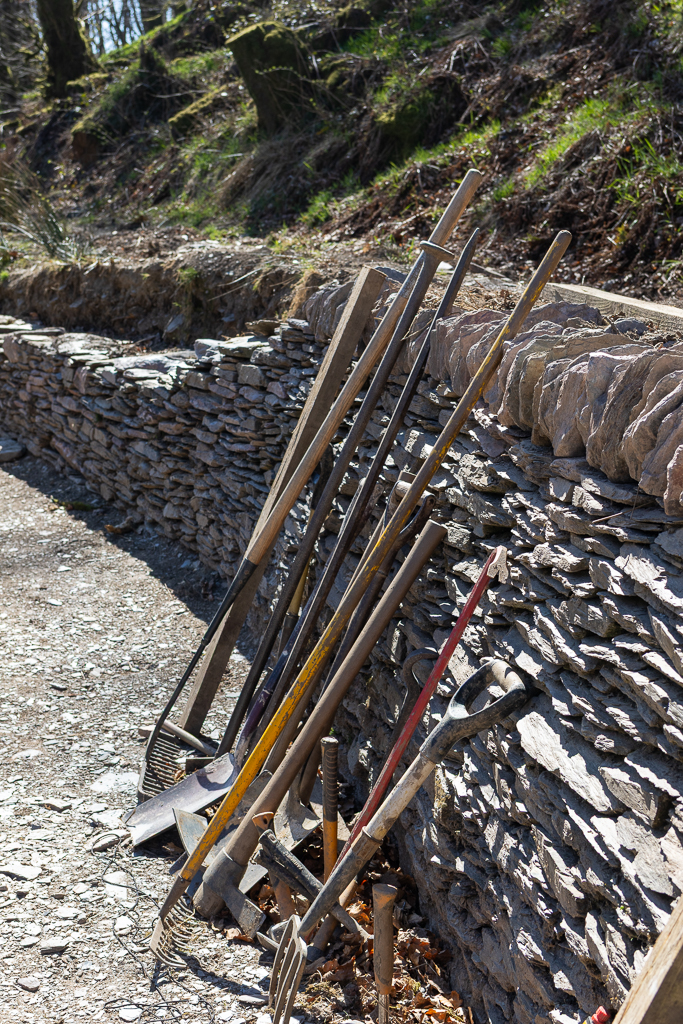 A selection of tools, rakes, spades and hooks lay up against a hand built Devon stone wall. This is part of the wild gardens project in Ashcombe Gardens in , Exmoor.