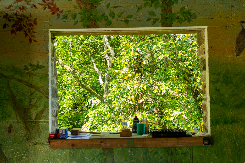 A hand painted mural on the inside of a log cottage in Peppercomber has been painted around a picturesque open window that looks out on to the trees and stream below