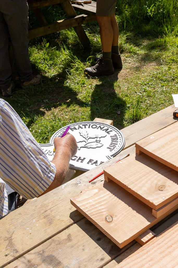 A volunteer from the National Trust is painting the lettering on the sign whilst sat in the sunshine.