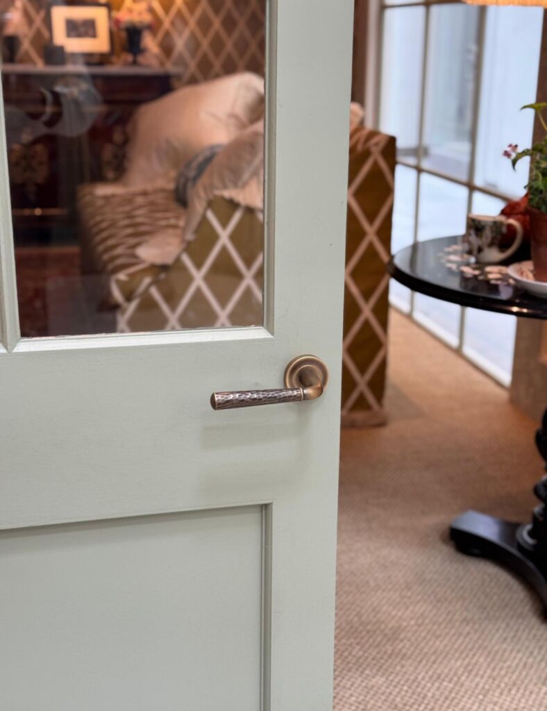 Photo shows a single door from a double door set with a hammered brass door lever on it. This door lever is handmade by Turnstyle Designs and finished in a Burnished Brass finish.