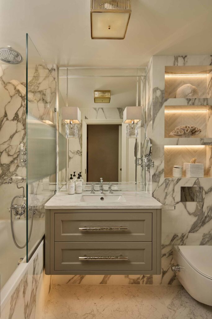 A stylish and luxury bathroom. The image focuses on the sink that has porcelain work tops with beige and gold tonal drawers. The drawers have hand hammered pull handles on each drawer, these are made by Turnstyle Designs.
