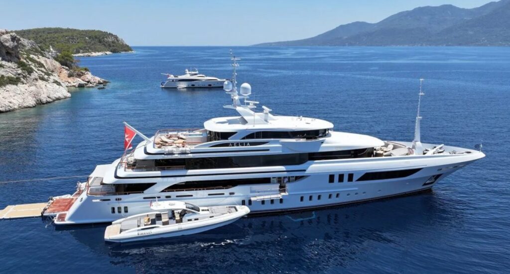 Image shows a large superyacht on the water, surrounded by the greek coastline.