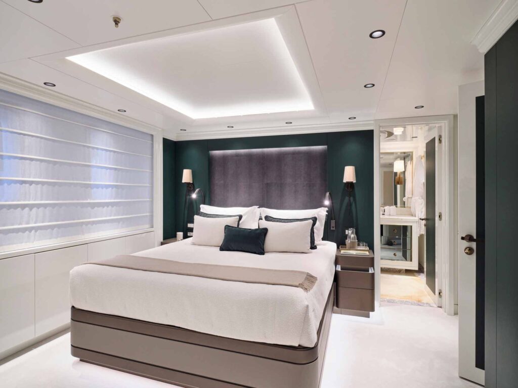 Large bed and luxury decorated room on a grand superyacht. The walls have a dark jade colour feature wall with luxury white bedding and decorative peices. Textured hardware by Turnstyle Designs has been used on the doors.