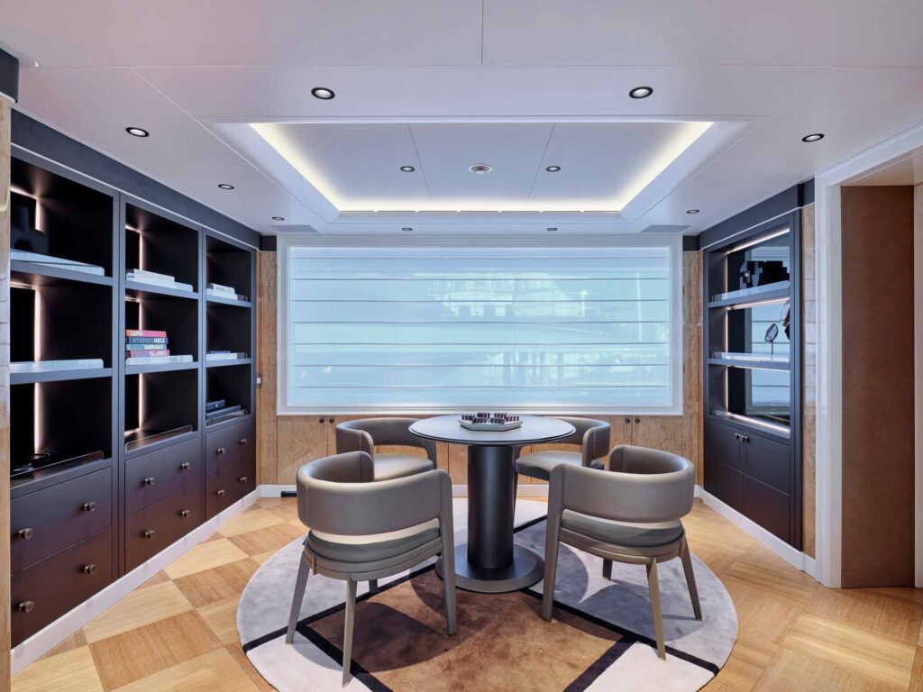 A luxury games room on a superyacht had a central table with bespoke furniture and units wither side. The room is a high end interior featuring luxury hardware by Turnstyle Designs on the cupabord doors.