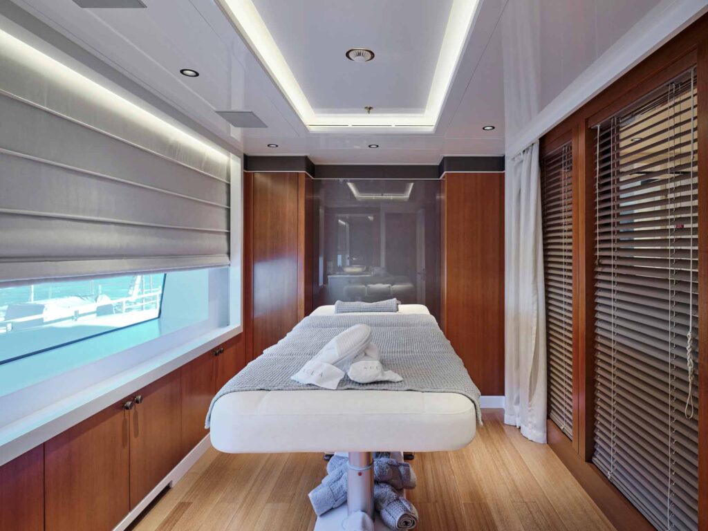 A treatment room for massage or facials on a luxury large super yacht. The bed is in the centre of the room with surrounding windows and cupboards. Decorative hardware by Turnstyle Designs has been used for the cabinet knobs which match the other areas on the yacht.