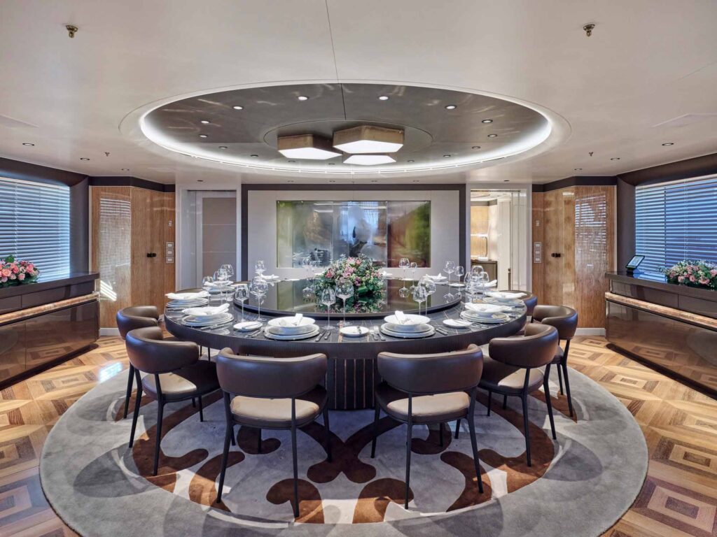 the inside interior of Motor yacht Aelia, a large superyacht. Image shows the luxury sky lounge dining area with huge round table and chairs all around. It is very opulent and luxury for high end charter clients.