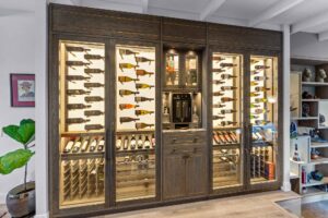 Luxury home wine cellar with custom glass-front cabinets, backlit wine storage, and dark wood cabinetry with Woven amalfine handmade handles by Turnstyle Designs.
