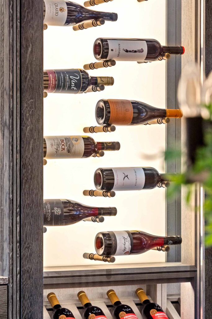 Wine bottles stacked in a high end luxury wine storage unit by Cellar Maison with backlit shelves and a dark oak finish.